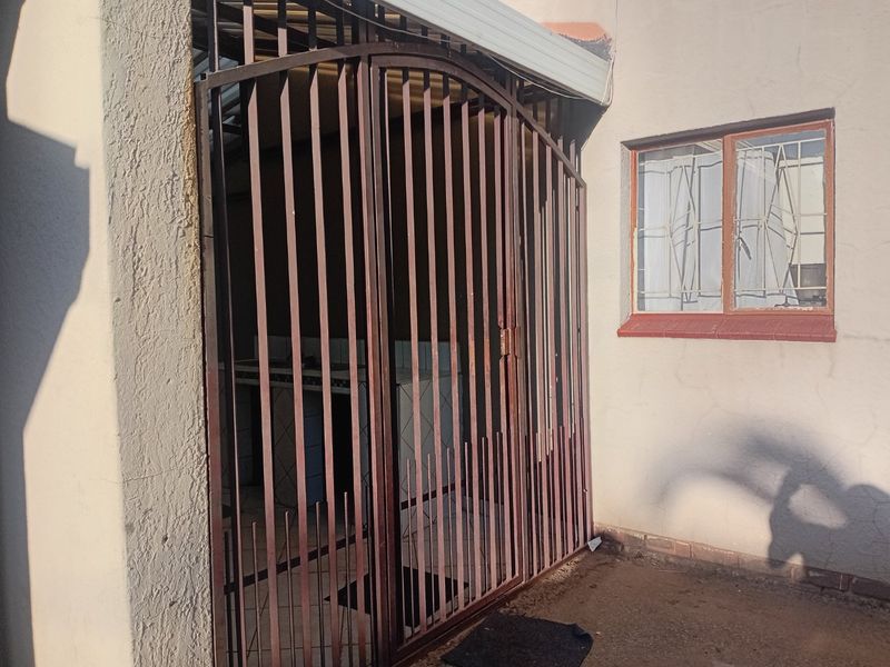 Rear exterior area featuring a security gate, window with security bars, and a built-in counter, showing signs of wear on the plaster and metalwork.