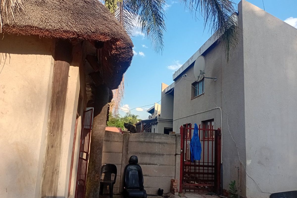 Rear exterior view of the townhouse property featuring a thatched roof structure, precast boundary wall, and metal gate access.