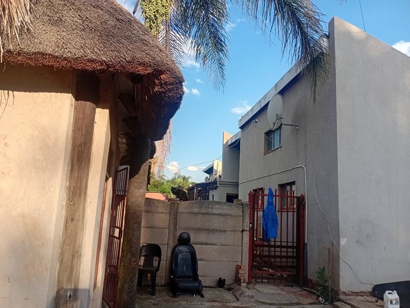Rear exterior view of the townhouse property featuring a thatched roof structure, precast boundary wall, and metal gate access.