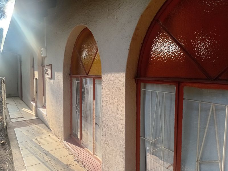 A rear exterior view of the townhouse featuring arched windows with security bars and a tiled patio area.