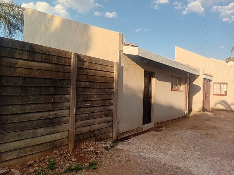 Rear exterior view of the townhouse featuring a precast concrete boundary wall, security gate, and basic paved area requiring maintenance.