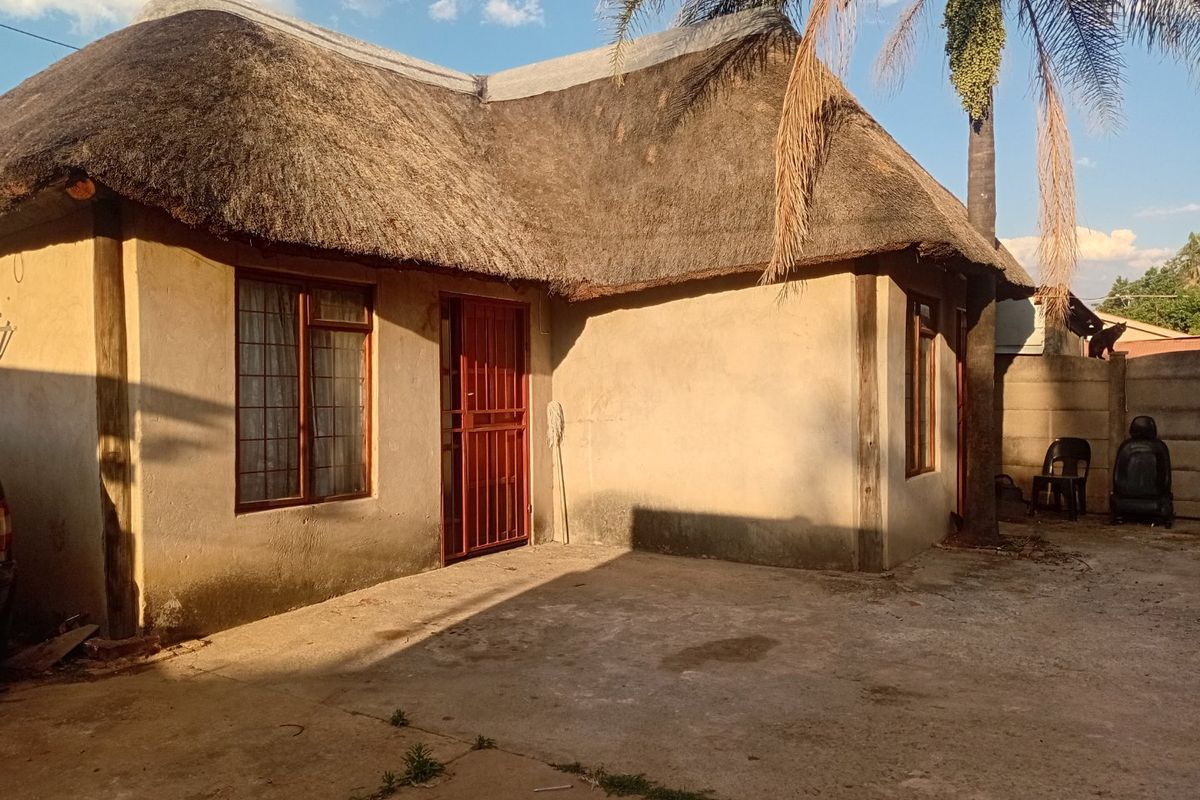 Front exterior view of a townhouse featuring a traditional thatch roof, concrete driveway, and security gate access.