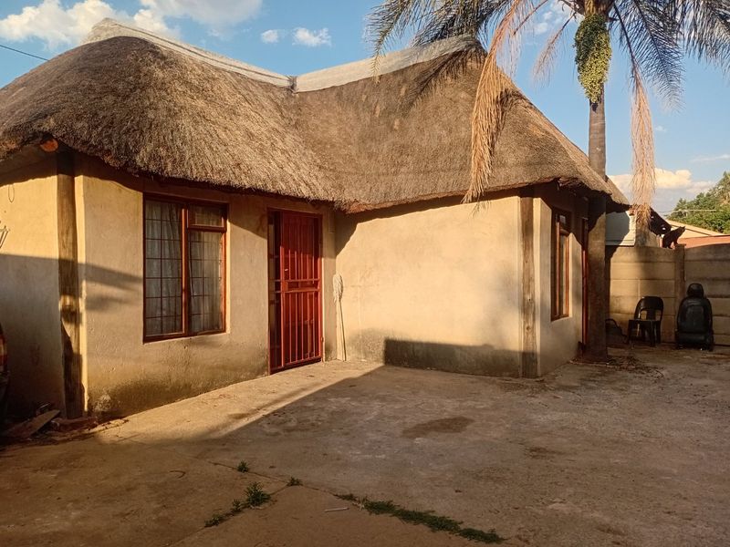 Front exterior view of a townhouse featuring a traditional thatch roof, concrete driveway, and security gate access.