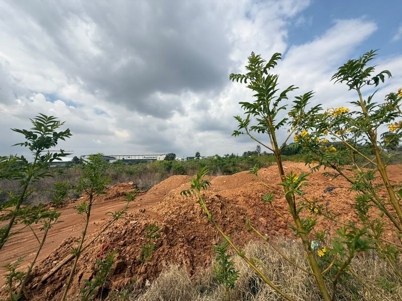 A view of an undeveloped residential plot featuring uneven earth mounds and natural vegetation under a cloudy sky.