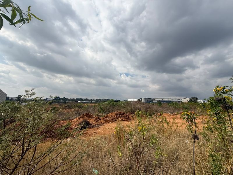 A view of an undeveloped residential land plot featuring natural vegetation and open space under a cloudy sky.