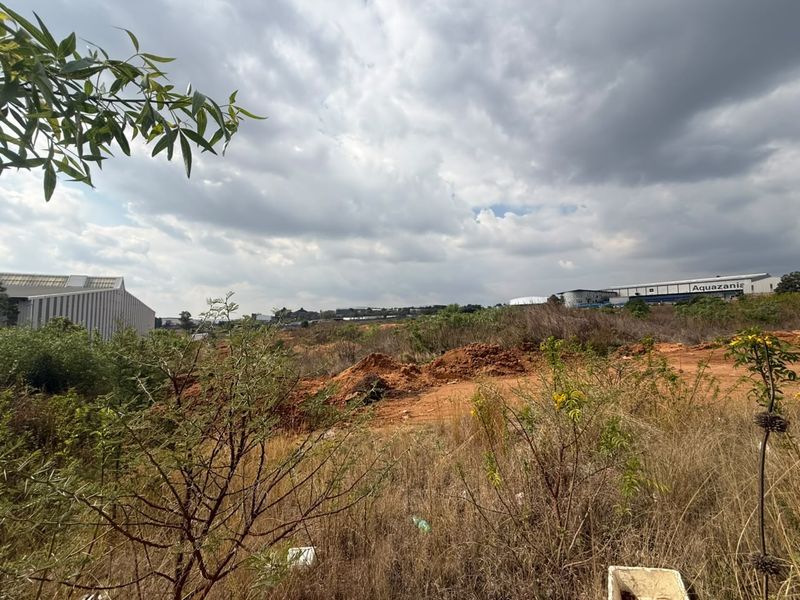 A view of an undeveloped residential land plot featuring natural vegetation and uneven terrain, situated in a developing area.