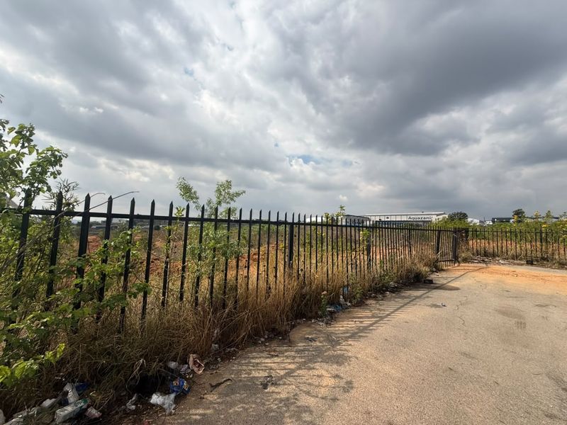 A view of the vacant residential land featuring metal security fencing along the paved road frontage.