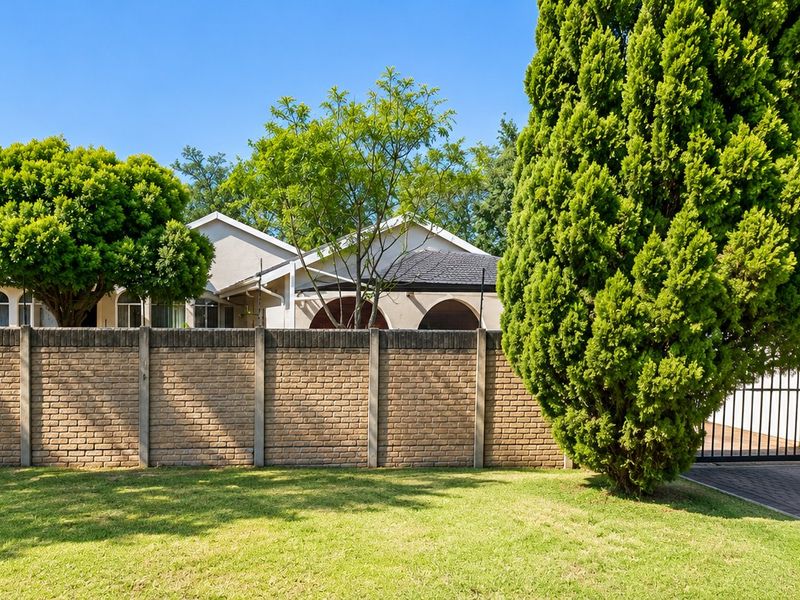 Front view of the property featuring a brick boundary wall, paved driveway, secure metal gate, and a glimpse of the house with a tiled roof.
