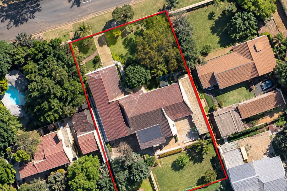Aerial view of a residential property featuring a tiled roof, solar panels, a paved driveway, and a spacious garden within a suburban setting.