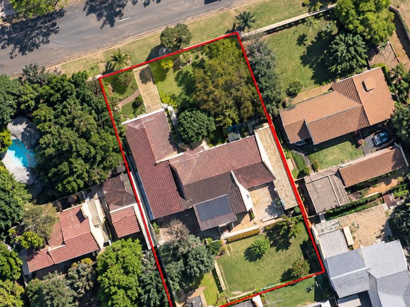 Aerial view of a residential property featuring a tiled roof, solar panels, a paved driveway, and a spacious garden within a suburban setting.