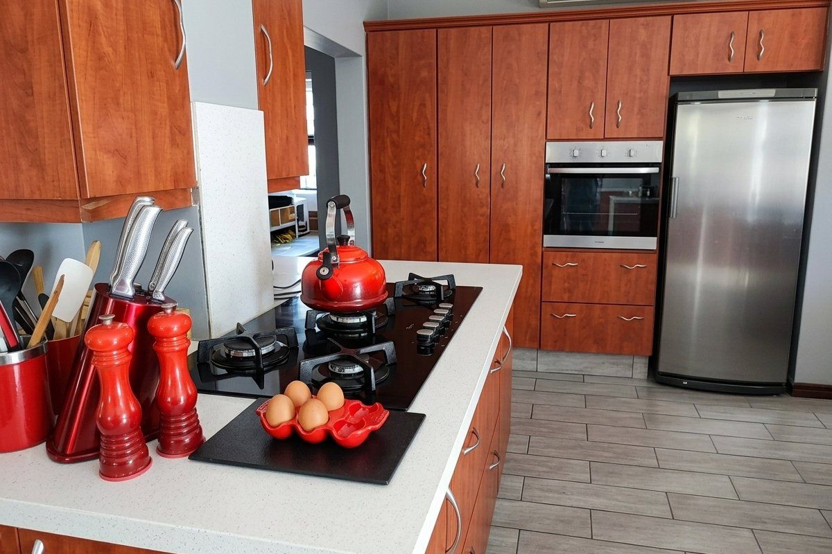 A well-maintained kitchen featuring warm-toned wooden cabinetry, stone countertops, a gas hob, and a built-in oven, complemented by modern tiled flooring.