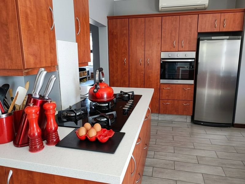 A well-maintained kitchen featuring warm-toned wooden cabinetry, stone countertops, a gas hob, and a built-in oven, complemented by modern tiled flooring.