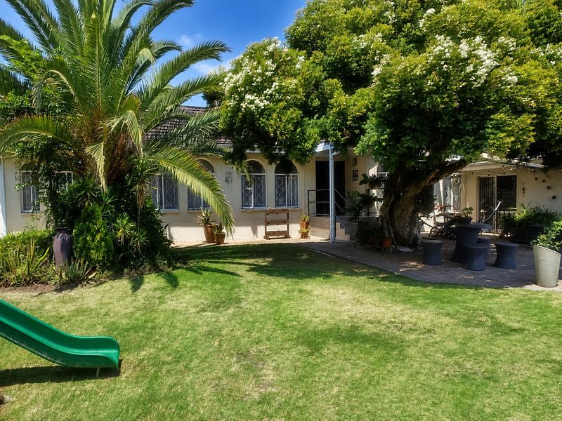 A spacious rear garden featuring a paved patio area, mature trees, and a well-maintained lawn, providing a pleasant outdoor living space.