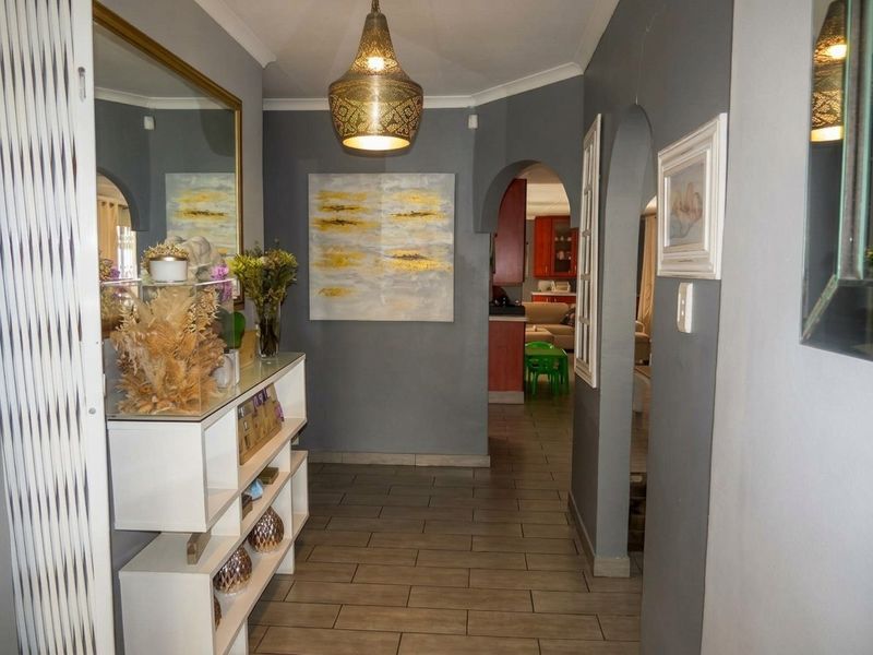 A well-maintained hallway featuring tiled flooring, arched architectural details, and a decorative pendant light fixture, providing access to adjacent living and kitchen areas.