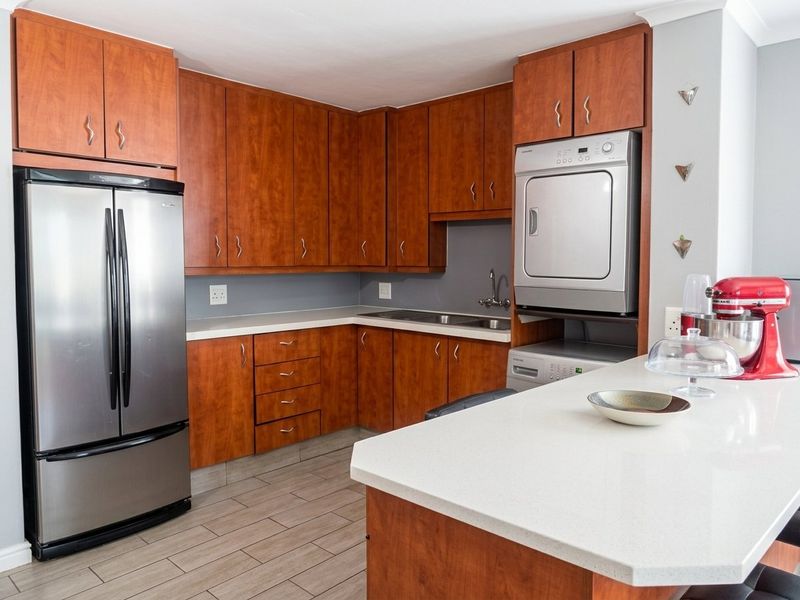 A functional kitchen featuring warm-toned cabinetry, stone countertops, and integrated laundry appliance housing, complemented by modern tiled flooring.