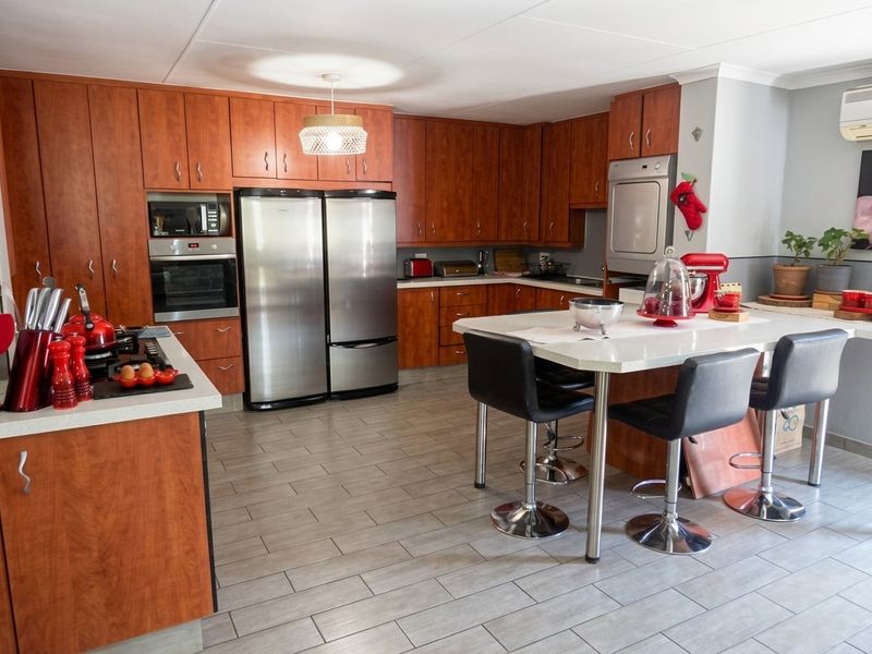 Spacious kitchen featuring warm-toned wooden cabinetry, stone countertops, a central island with seating, and modern tiled flooring.