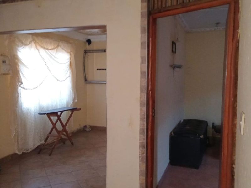 A view of a hallway connecting to adjacent rooms, featuring tiled flooring and dated wall finishes in need of cosmetic updates.