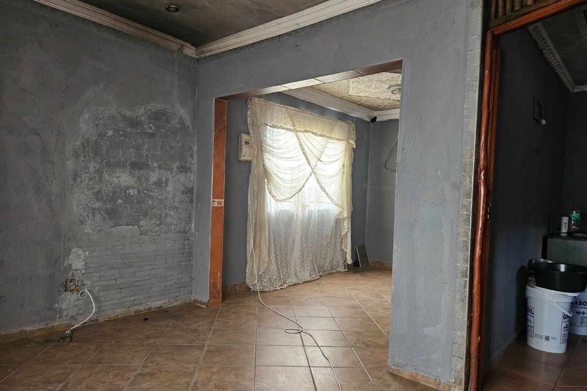 An empty living area featuring tiled flooring and an archway, currently requiring significant wall and ceiling repairs and cosmetic updates.