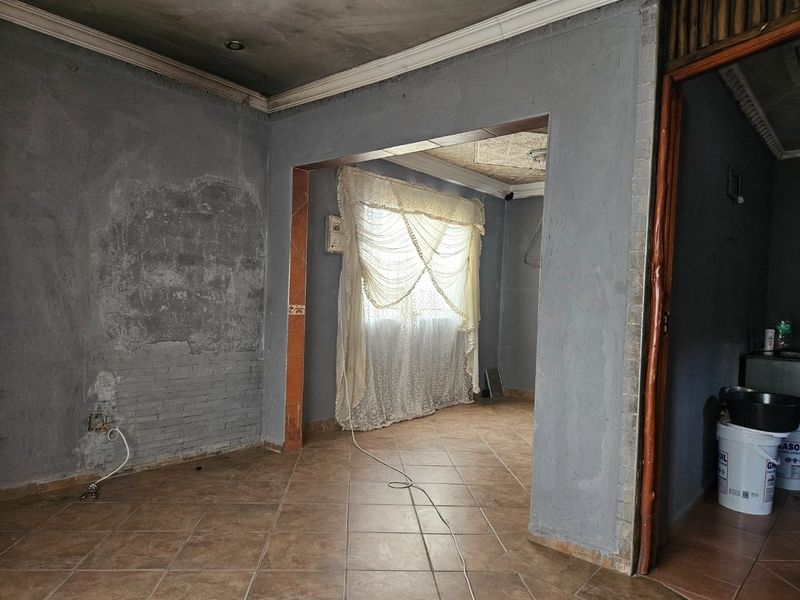 An empty living area featuring tiled flooring and an archway, currently requiring significant wall and ceiling repairs and cosmetic updates.