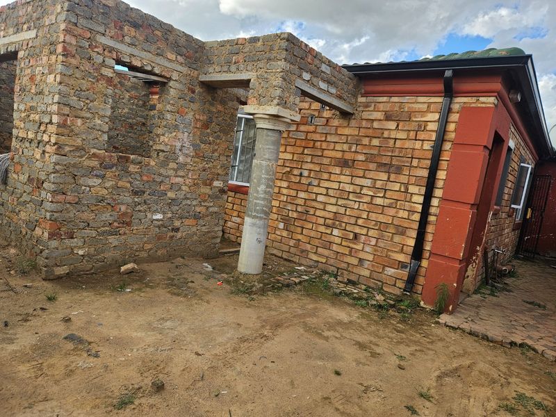 Rear exterior view of a property showing an unfinished brick extension with a concrete support column and exposed masonry work.