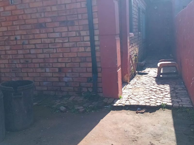 A side exterior view of the property featuring a brick facade, paved walkway, and basic drainage infrastructure.