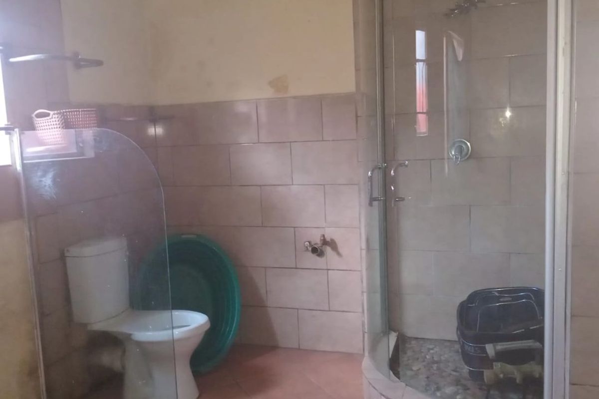 A bathroom featuring a corner shower enclosure, toilet, and tiled finishes. The space requires cosmetic updates to the wall surfaces.