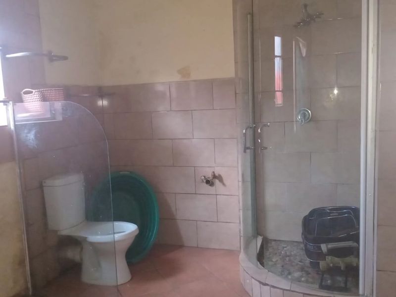 A bathroom featuring a corner shower enclosure, toilet, and tiled finishes. The space requires cosmetic updates to the wall surfaces.