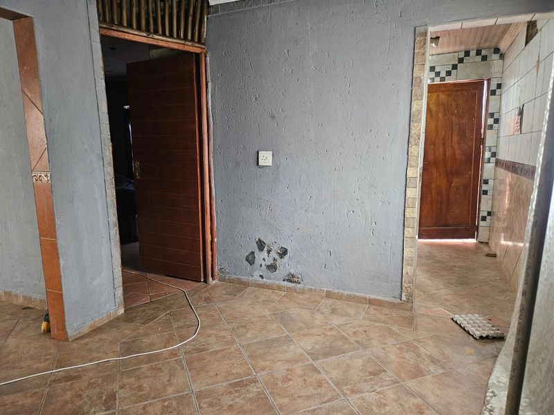 A vacant hallway featuring tiled flooring and wooden door frames, showing visible signs of wall surface damage and wear.