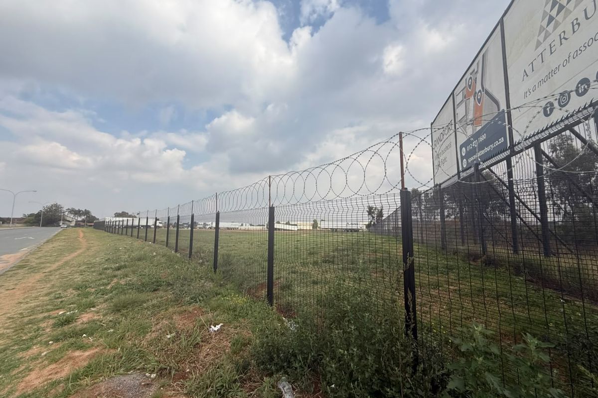A vacant residential land plot secured with mesh fencing and razor wire, featuring a prominent advertising billboard along the street frontage.