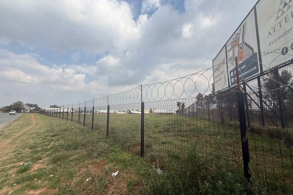 A vacant residential land plot secured with mesh perimeter fencing and razor wire, featuring a large advertising billboard on the property boundary.