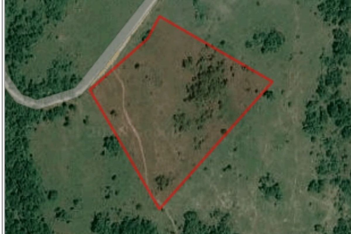 Aerial view of a vacant residential plot outlined in red, showing natural terrain and proximity to an access road.