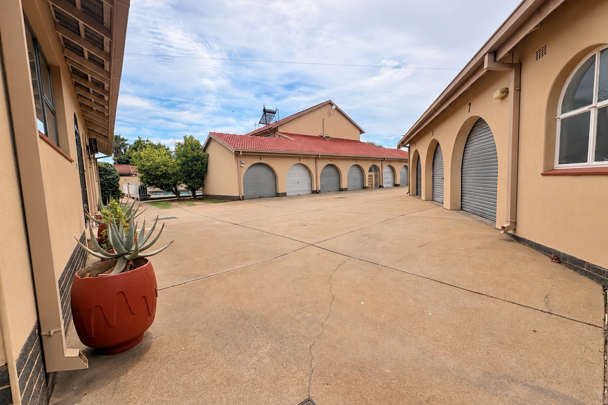A paved courtyard area featuring multiple garage units with arched entrances, a tiled roof structure, and integrated solar water heating system.