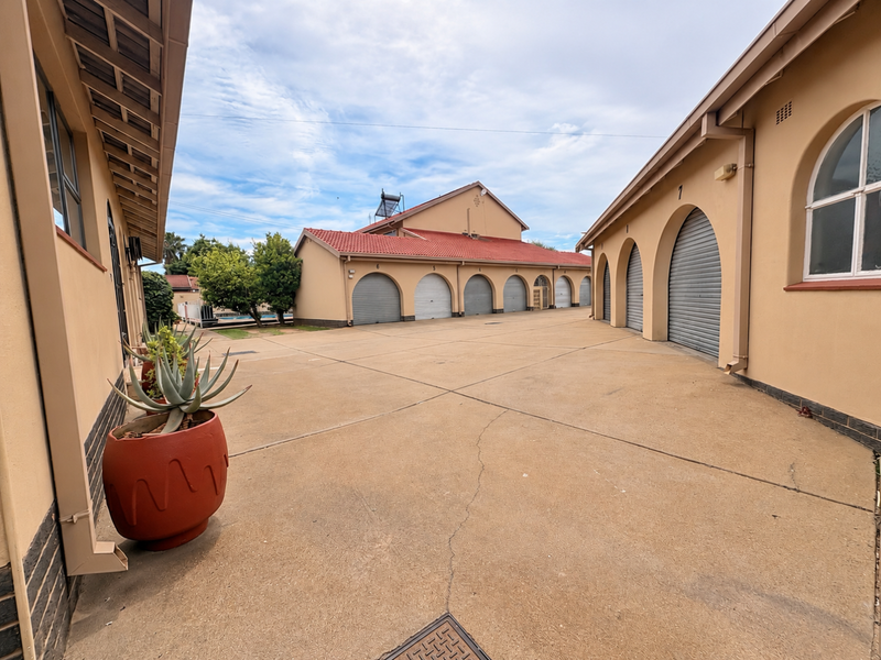 A paved courtyard area featuring multiple garage units with arched entrances, a tiled roof structure, and integrated solar water heating system.
