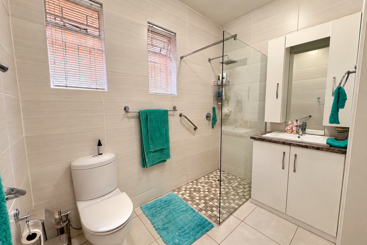 Modern bathroom featuring a walk-in shower with glass screen, vanity cabinet with basin, and neutral wall and floor tiling.