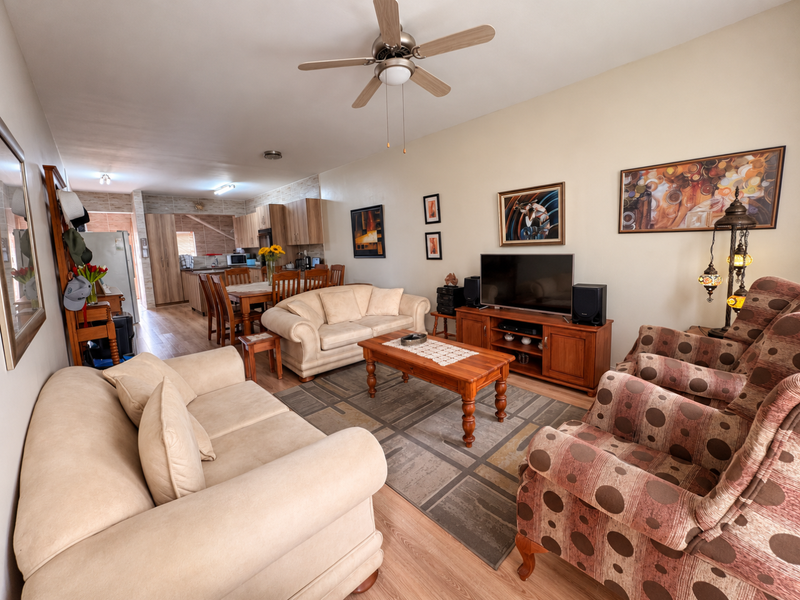 Spacious open-plan living and dining area featuring laminate flooring, a ceiling fan, and an adjoining kitchen with built-in cabinetry.
