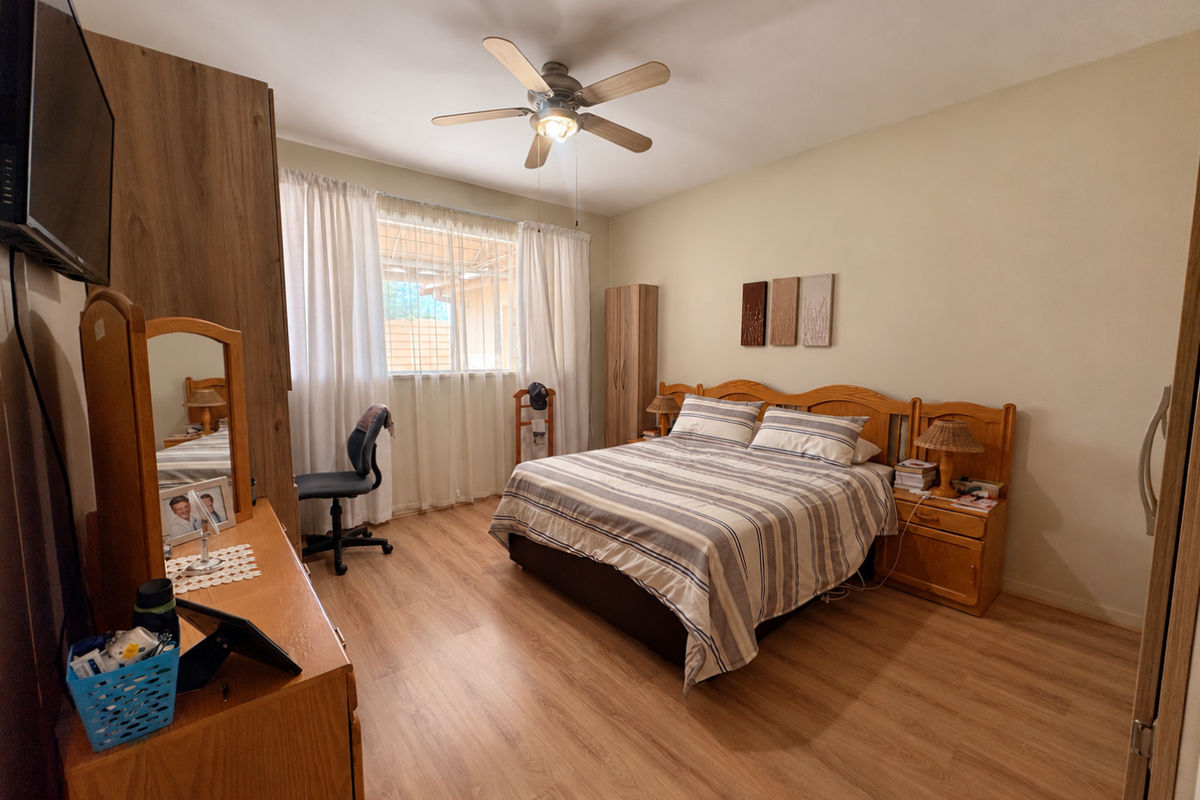 A well-maintained bedroom featuring laminate flooring, a ceiling fan, and built-in wardrobe storage, offering a functional and comfortable living space.