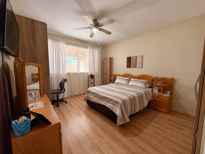 A well-maintained bedroom featuring laminate flooring, a ceiling fan, and built-in wardrobe storage, offering a functional and comfortable living space.