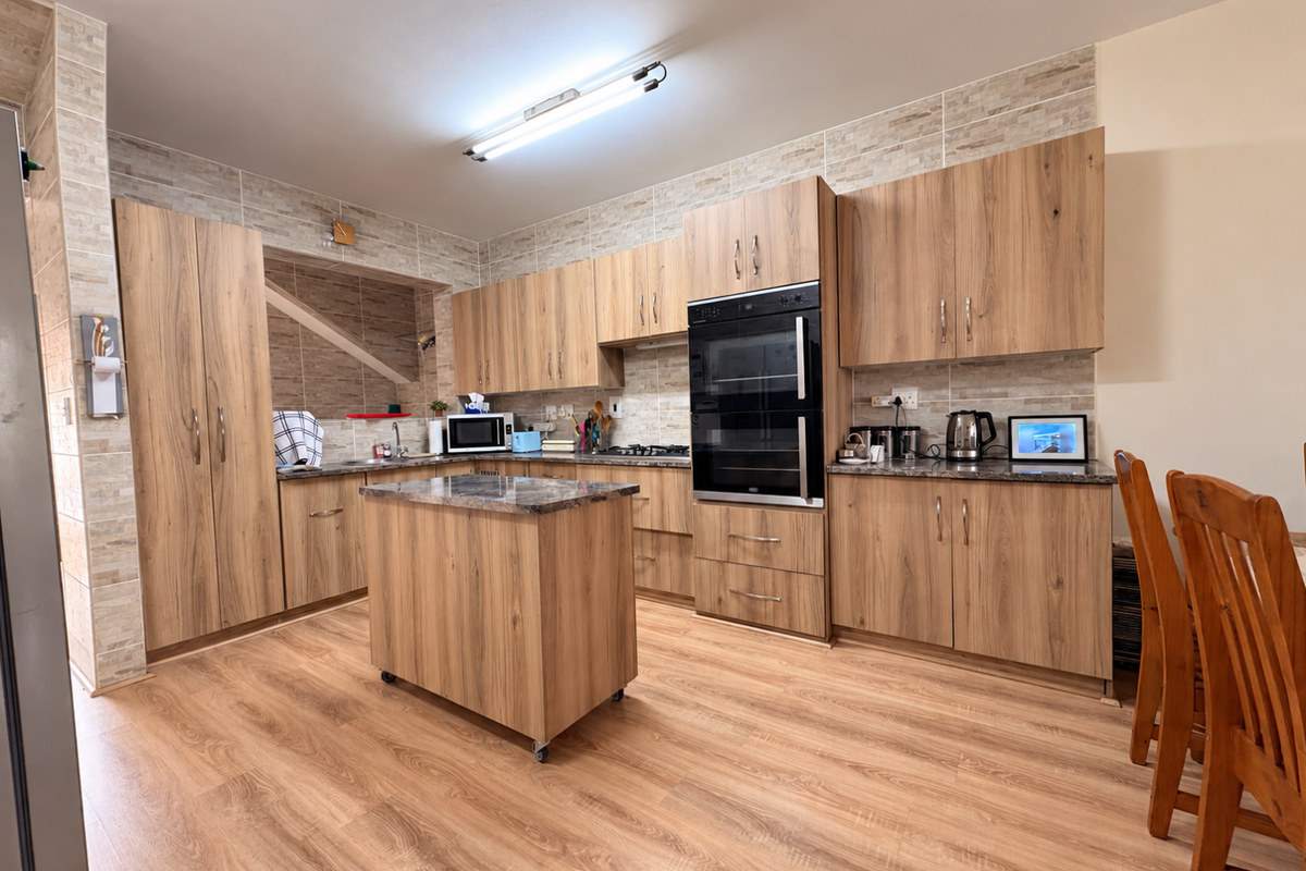 A well-maintained kitchen featuring wood-grain cabinetry, stone-look countertops, a built-in double oven, and a matching kitchen island with laminate flooring throughout.