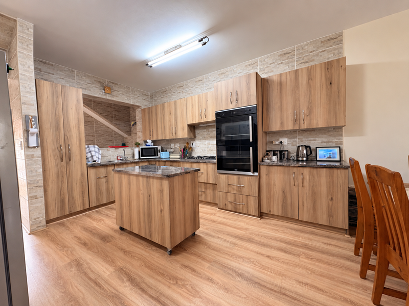 A well-maintained kitchen featuring wood-grain cabinetry, stone-look countertops, a built-in double oven, and a matching kitchen island with laminate flooring throughout.
