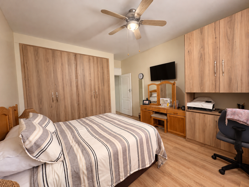 A well-maintained bedroom featuring extensive built-in wooden cabinetry, laminate flooring, and a central ceiling fan, offering ample storage and a functional layout.