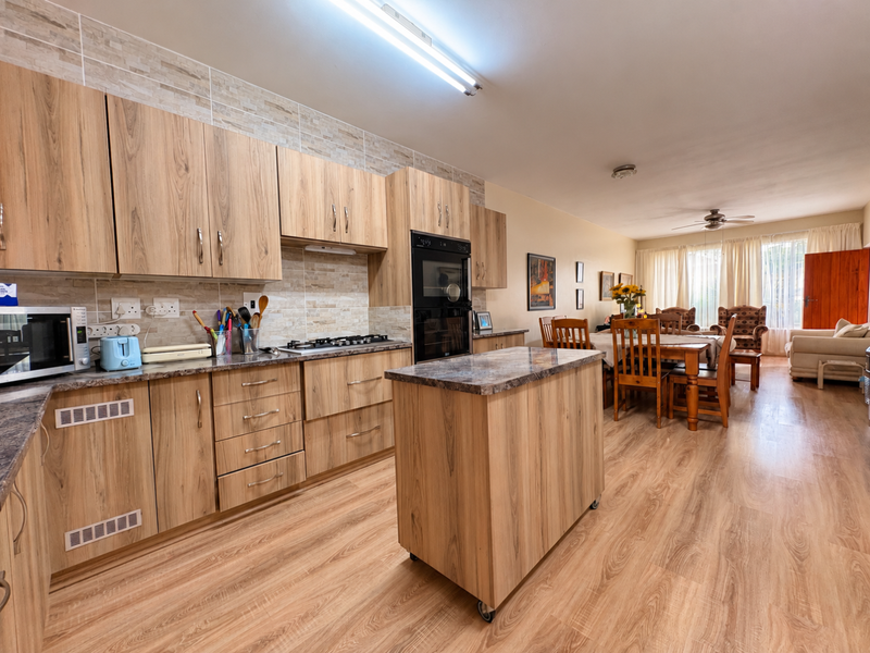 Spacious open-plan kitchen and dining area featuring wood-look cabinetry, stone-look countertops, built-in oven, gas hob, and durable laminate flooring throughout.