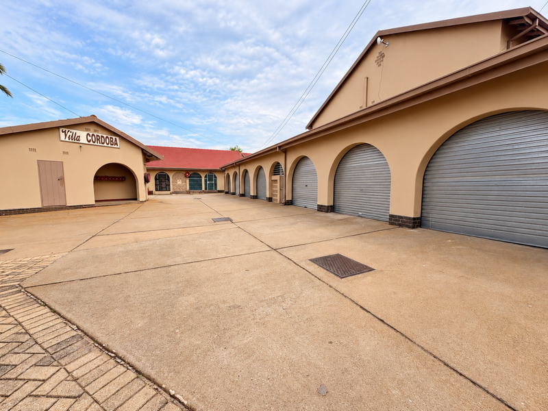 A well-maintained exterior courtyard featuring multiple secure roller shutter garage doors and a spacious concrete driveway within the Villa Cordoba complex.