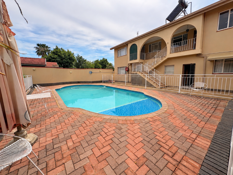 A communal pool area featuring paved decking, metal safety fencing, and access to the apartment building's exterior staircase and arched balconies.