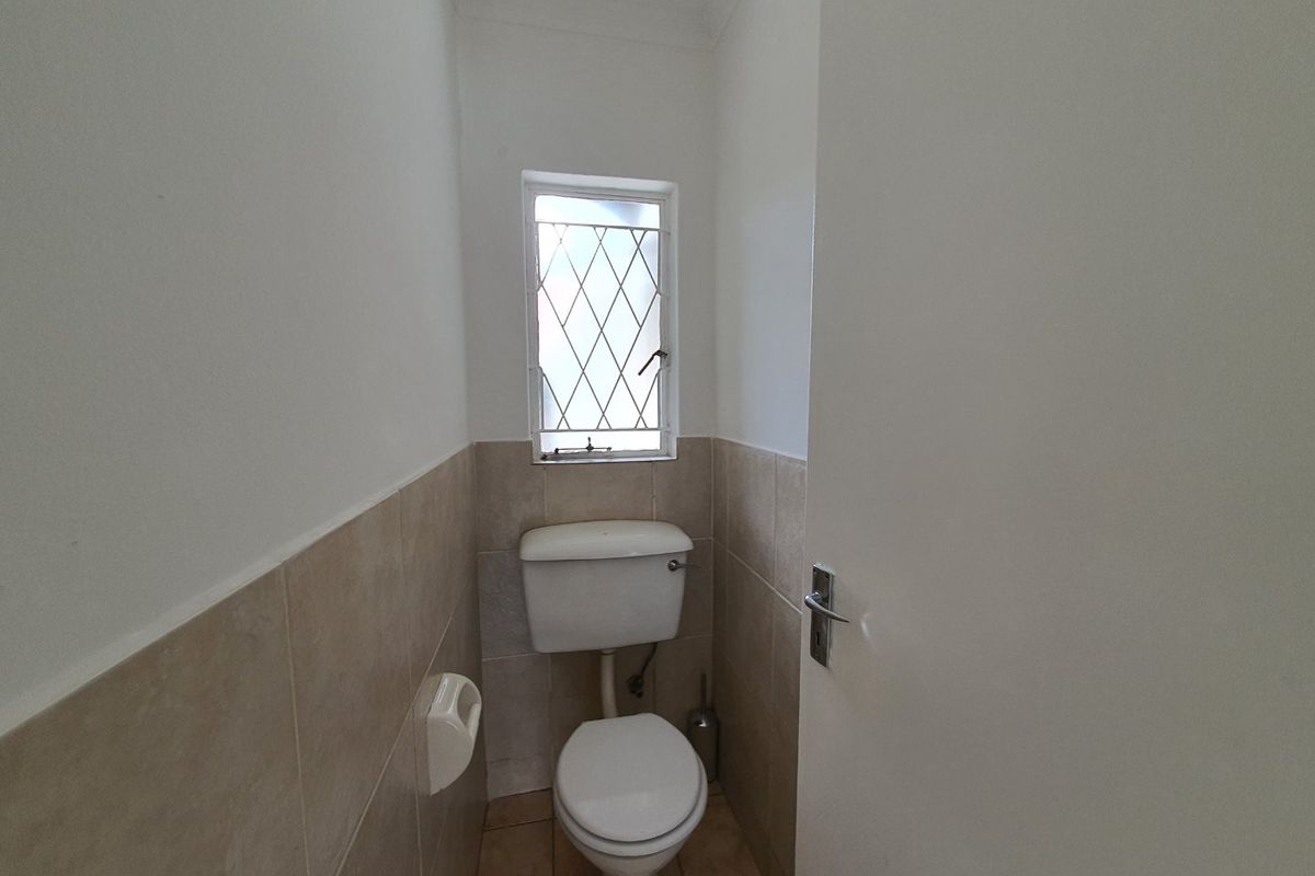 A compact guest toilet featuring neutral ceramic wall and floor tiles, a white toilet suite, and a leaded glass window.