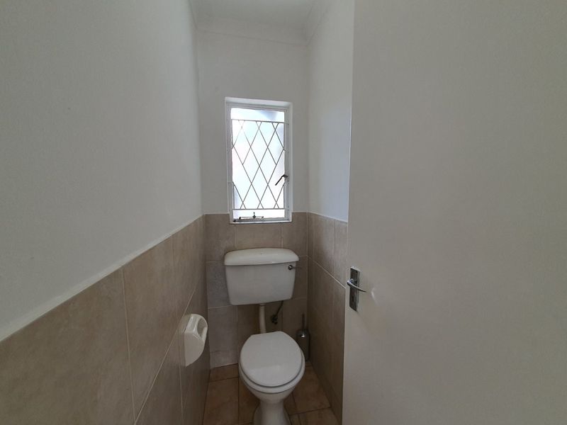 A compact guest toilet featuring neutral ceramic wall and floor tiles, a white toilet suite, and a leaded glass window.