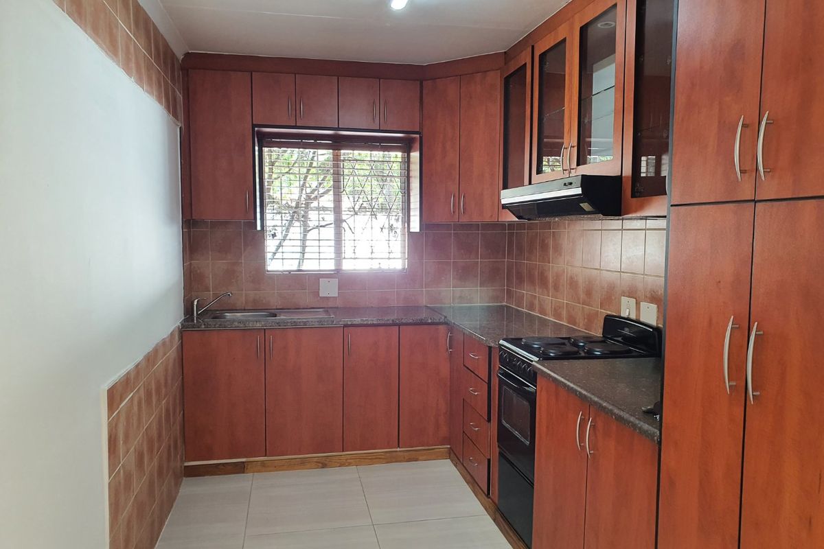 A functional kitchen featuring wood-finish cabinetry, tiled backsplash, granite-look countertops, and integrated appliances including an oven and extractor fan.