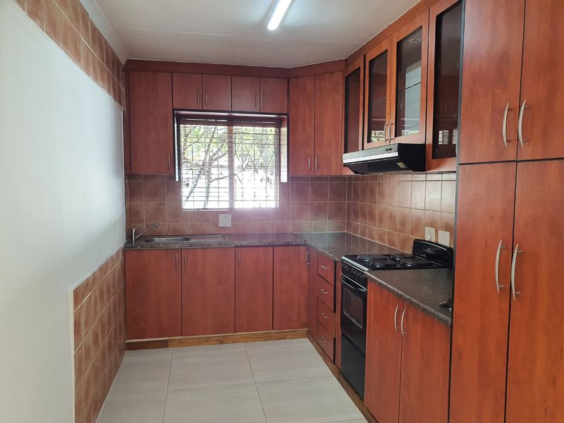 A functional kitchen featuring wood-finish cabinetry, tiled backsplash, granite-look countertops, and integrated appliances including an oven and extractor fan.