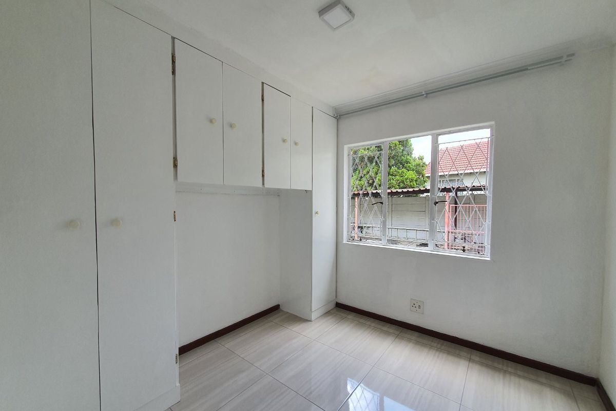 A clean, empty bedroom featuring neutral tiled flooring, built-in white cabinetry, and a window with security bars.