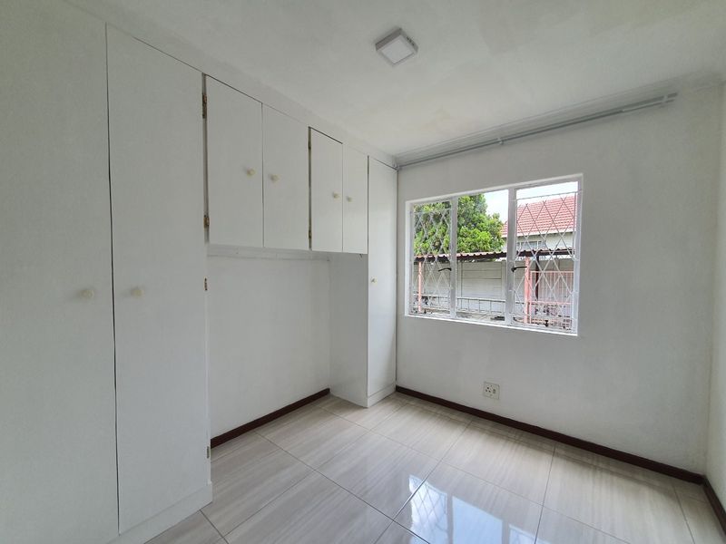 A clean, empty bedroom featuring neutral tiled flooring, built-in white cabinetry, and a window with security bars.