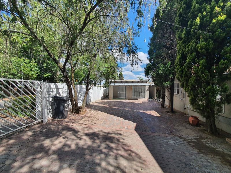 A paved driveway leading to the front entrance of the property, featuring perimeter fencing and mature trees.
